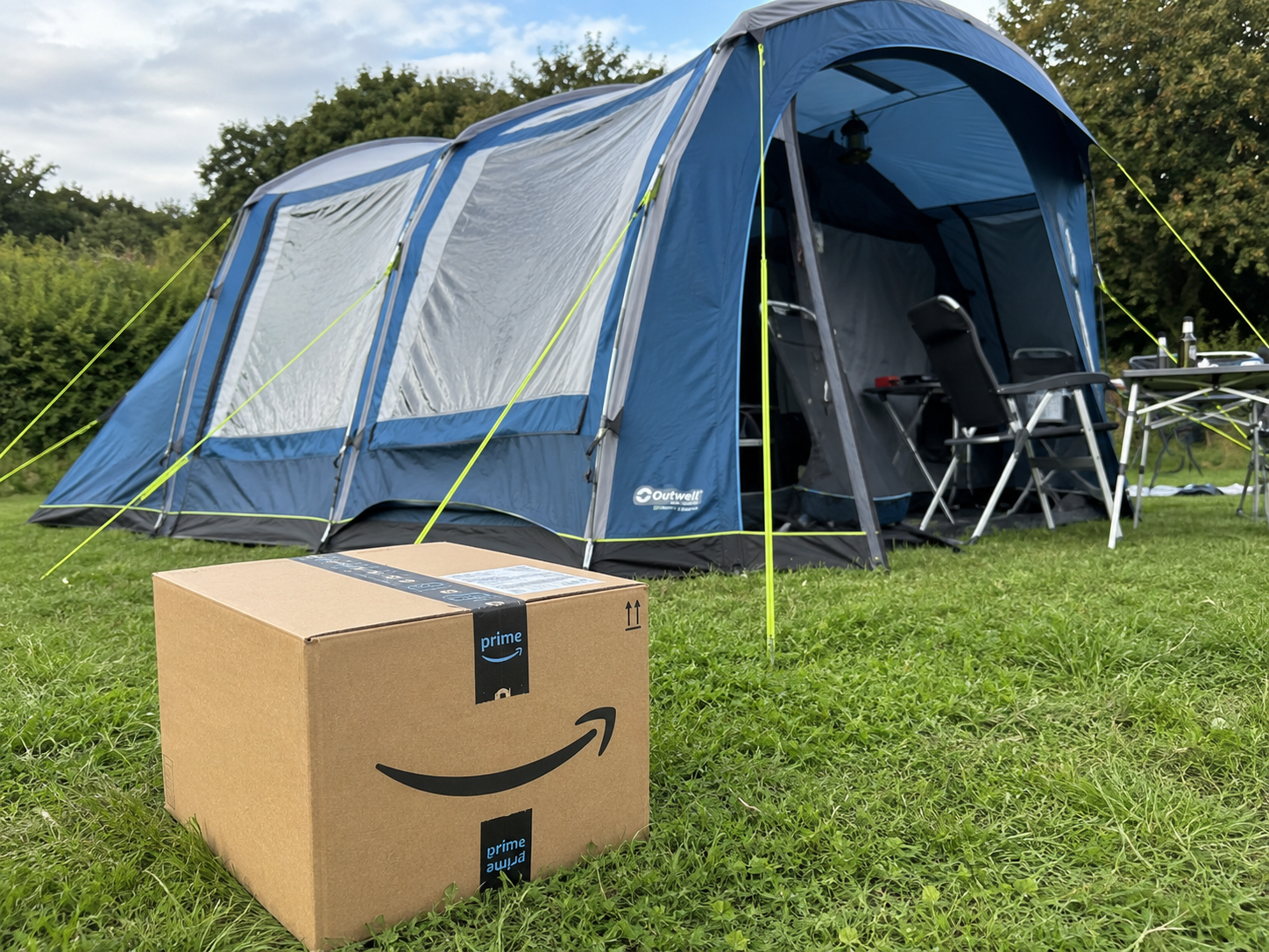 Caja de un paquete de Amazon entregado junto a una tienda de campaña familiar montada en un terreno de hierba.